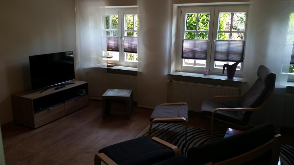 uma sala de estar com um sofá e uma televisão e duas janelas em Ferienwohnung Gartenblick em Westerstede