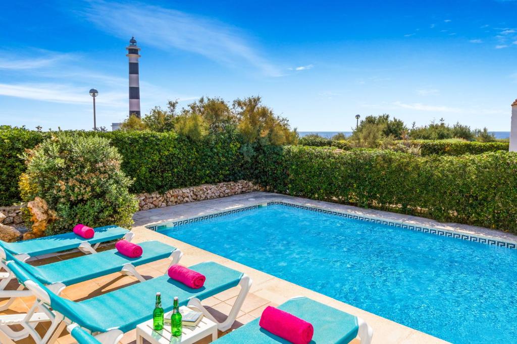 a swimming pool with lounge chairs and a lighthouse at Villa FARO by Mauter Villas in Cala en Bosc