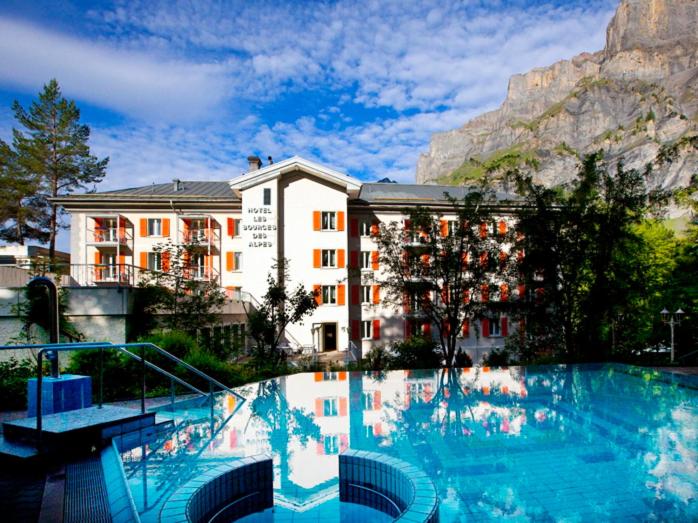 a hotel with a large swimming pool in front of a mountain at Hôtel Les Sources des Alpes in Leukerbad