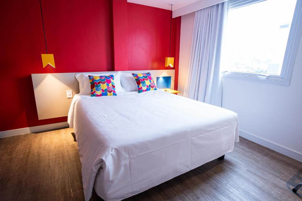 um quarto com uma grande cama branca com paredes vermelhas em ibis Styles Campina Grande em Campina Grande