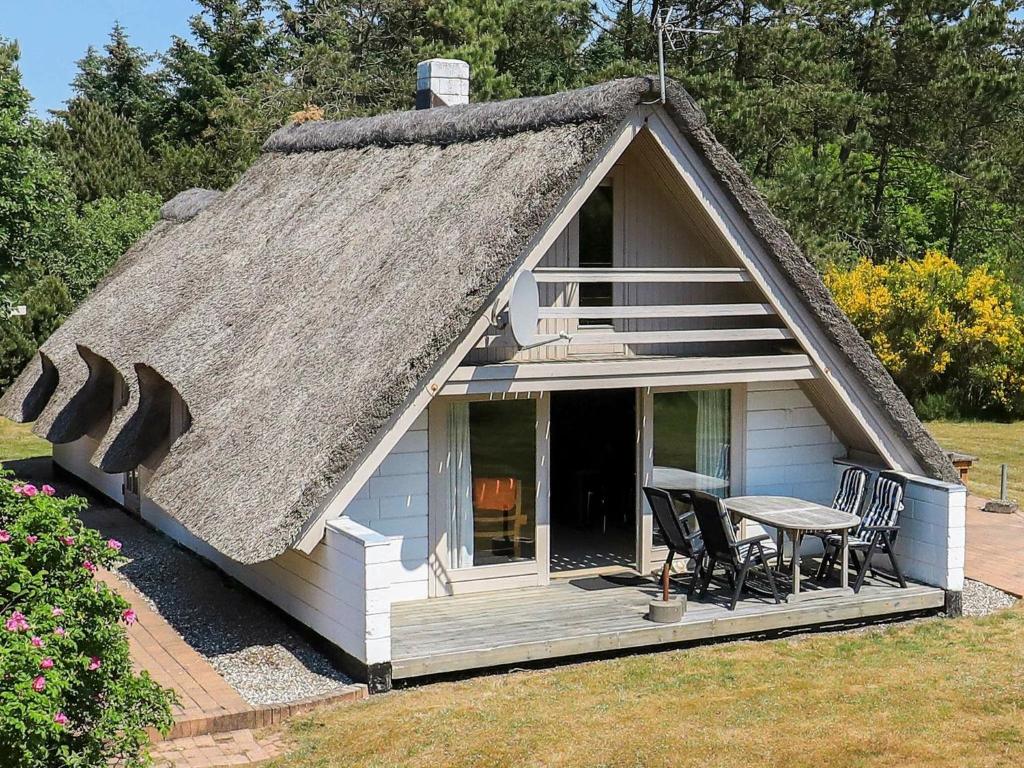 a small house with a thatched roof with a table and chairs at Holiday Home Fyrrealle in Nørby