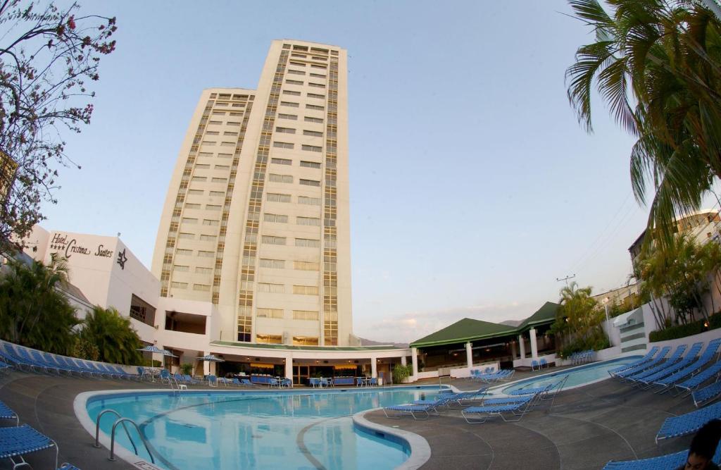 a building with a swimming pool in front of a building at Hotel Cristina Suites in Puerto La Cruz