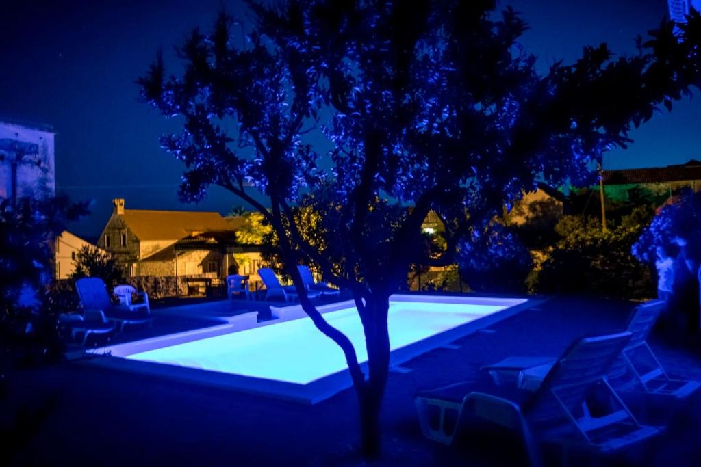 una piscina con sillas y un árbol por la noche en Vacation house near sea & beaches with HEATED POOL & BBQ, en Orebić