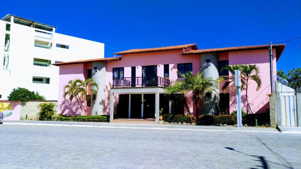 Itaobim的住宿－Brisa Do Vale Pousada，一条街道前方棕榈树的粉红色建筑
