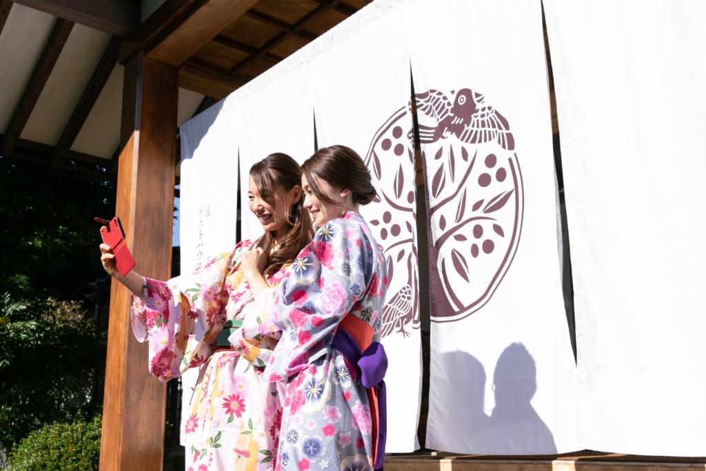 Due donne in kimono in piedi accanto a una bandiera di Onsen Guest House Aobato no Su a Matsue