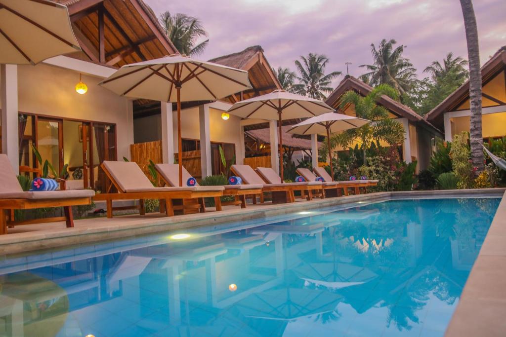 una piscina en un complejo con sillas y sombrillas en Cozy Cottages Lombok en Senggigi 