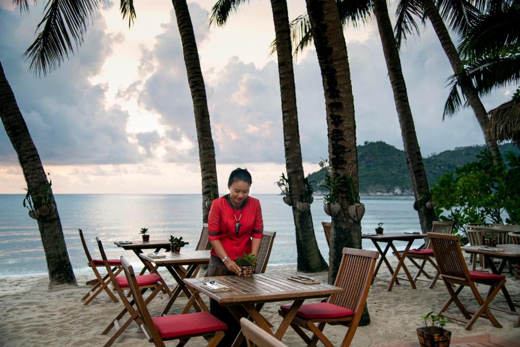 a woman sitting at a table with a laptop on the beach at Anantara Rasananda Koh Phangan Villas in Thong Nai Pan Noi