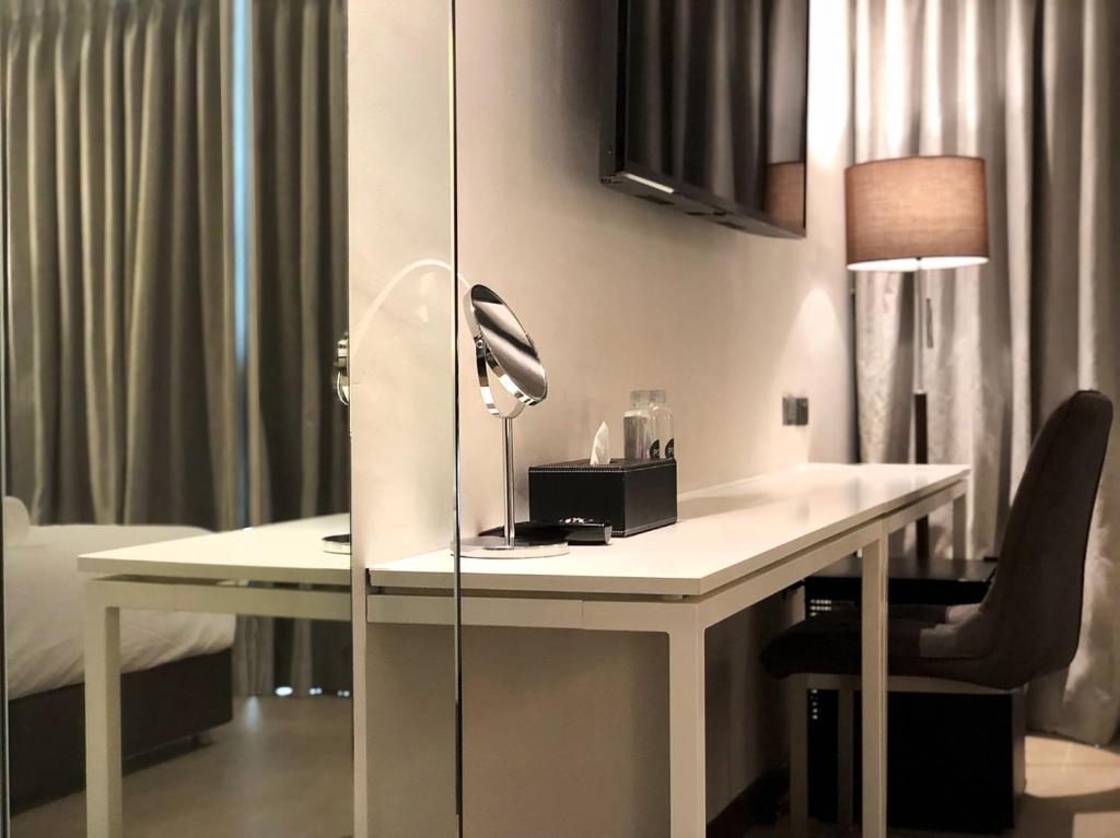 A long white desk with a chair, grooming mirror, lamp, and television above it.