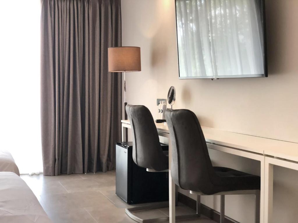 A two-chair desk area sits beside the curtained window and beneath a wall-mounted TV.