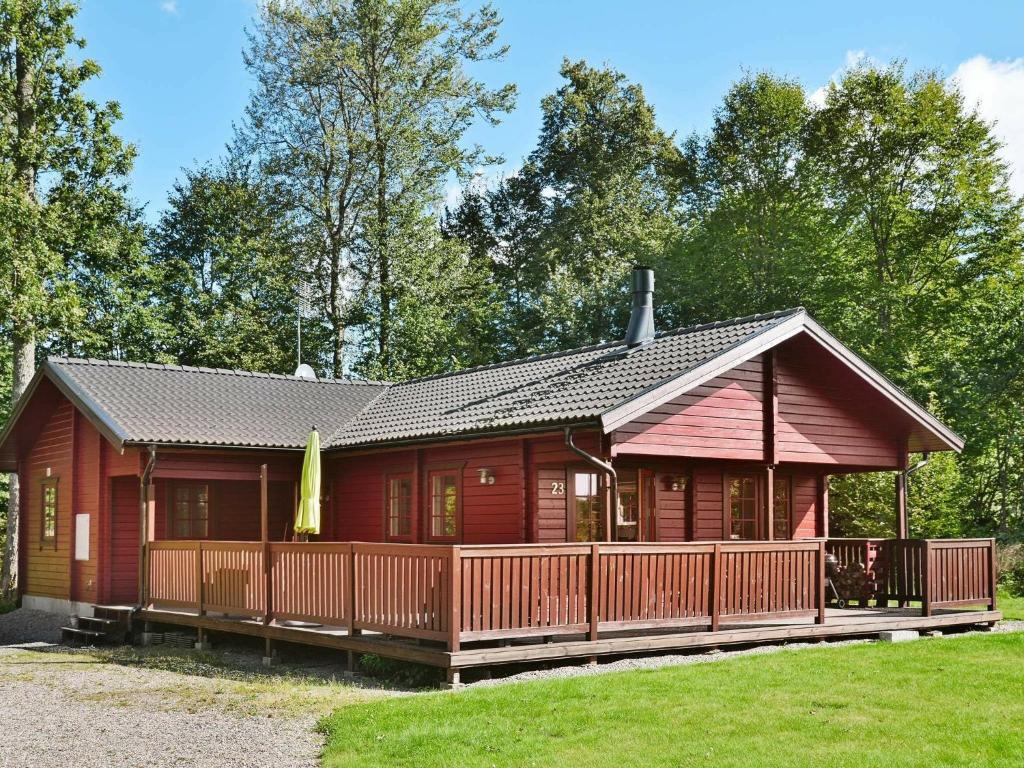 a red cabin with a wooden deck in the grass at Three-Bedroom Holiday home in Hästveda in Hästveda