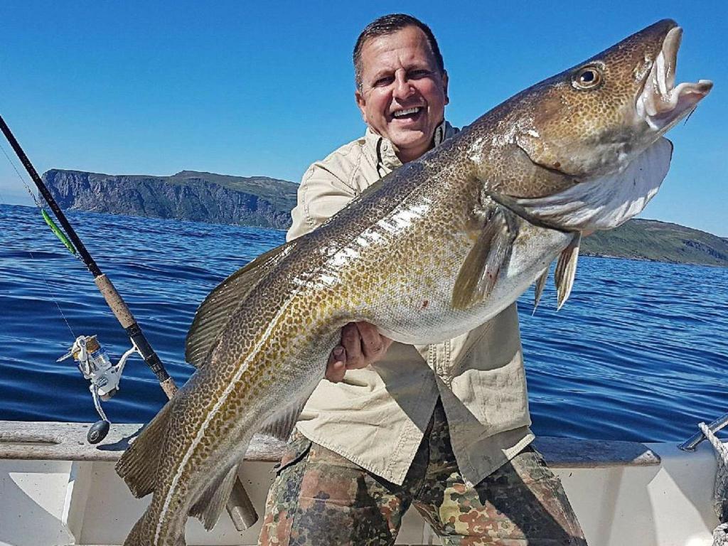 um homem segurando um peixe grande em um barco em Holiday Home Breivikbotn em Vatna