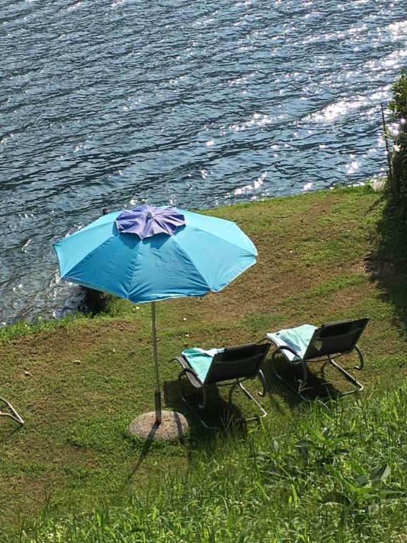 zwei Stühle und ein Regenschirm neben dem Wasser in der Unterkunft La Rivetta in Omegna