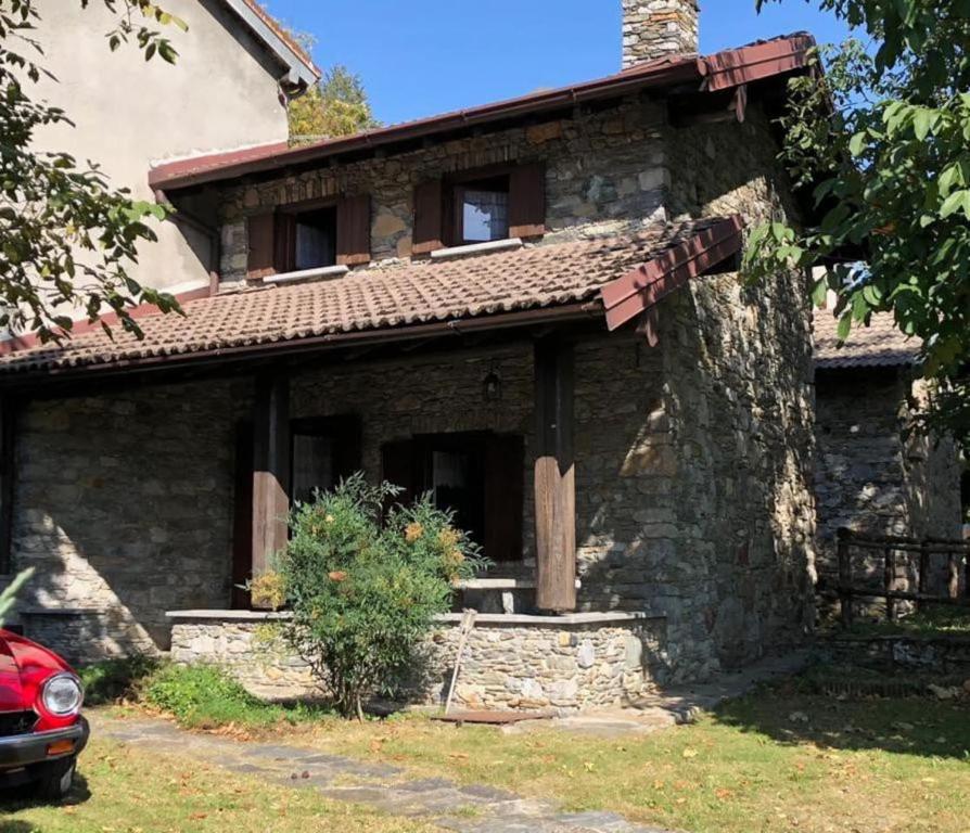 une maison en pierre avec une voiture rouge garée devant elle dans l'établissement Baita Agostina, à Gravedona