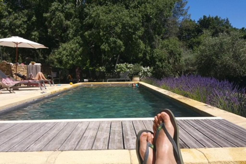 a person with their feet up next to a swimming pool at le mas du cypres, 12 pers et piscine in Aigaliers