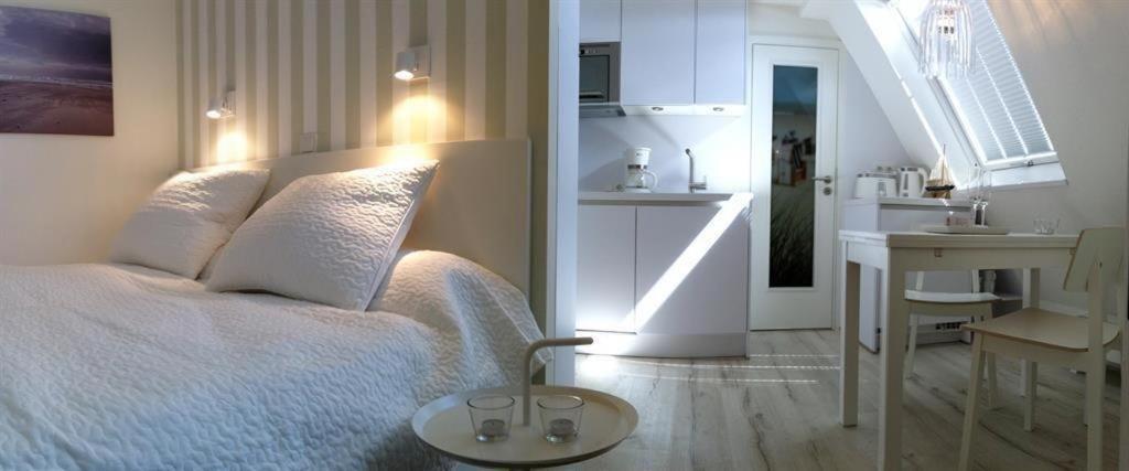 ヴェスターラントにあるHaus-LIV-Appartement-Dueneの白いベッドルーム(ベッド1台付)、キッチンが備わります。