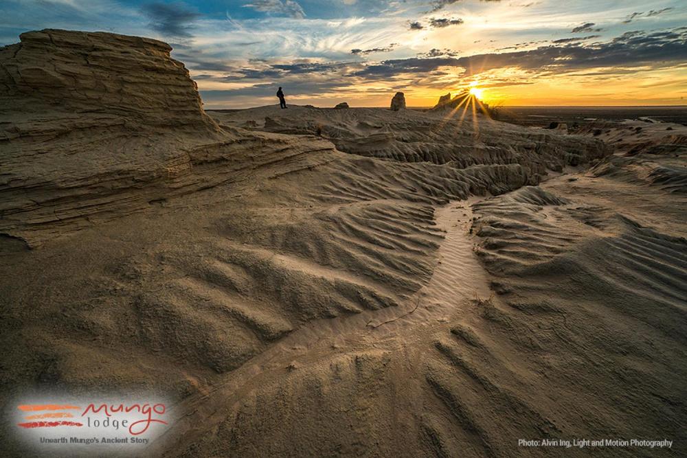 a person standing in a desert with the sun setting at Mungo Lodge in Mungo