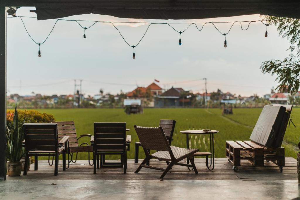 a group of chairs and tables on a patio with a field at Big Brother Surf Inn in Canggu