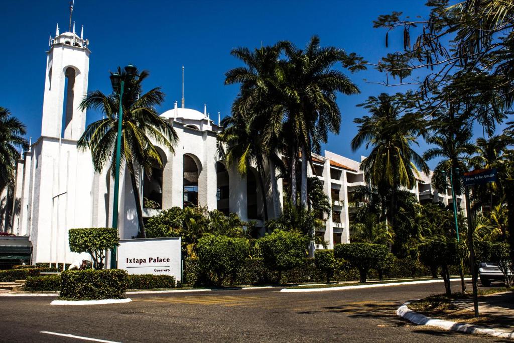un bâtiment blanc avec une tour d'horloge et des palmiers dans l'établissement Ixtapa Palace, à Ixtapa