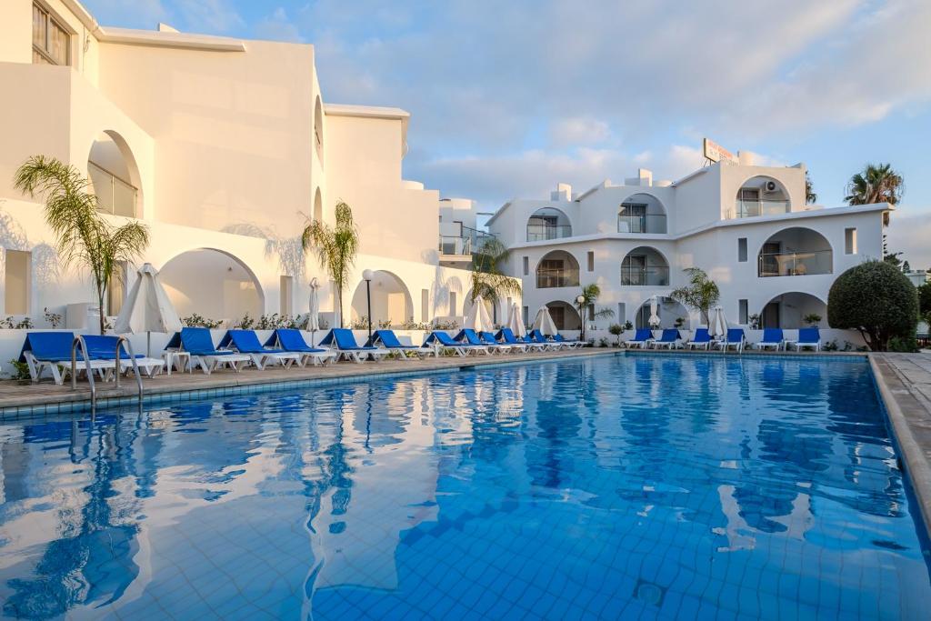 a swimming pool in front of a resort with blue chairs at Pandream Hotel Apartments in Paphos City