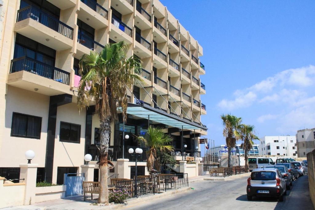 un edificio con palme di fronte a una strada di Canifor Hotel a San Pawl il-Baħar