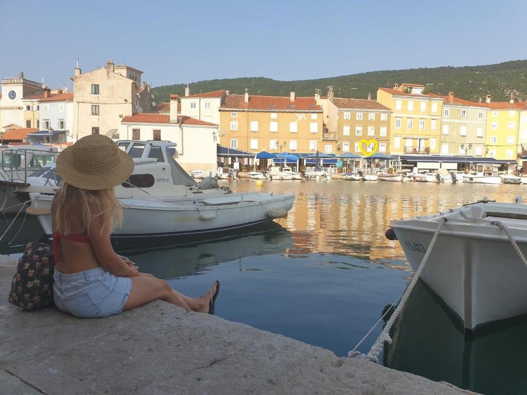 Una donna seduta su un molo che guarda le barche in un porto. di Apartment Filipas a Cres