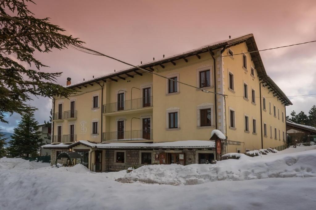 a large yellow building with snow around it at Relais Ducale Spa & Pool in Pescocostanzo