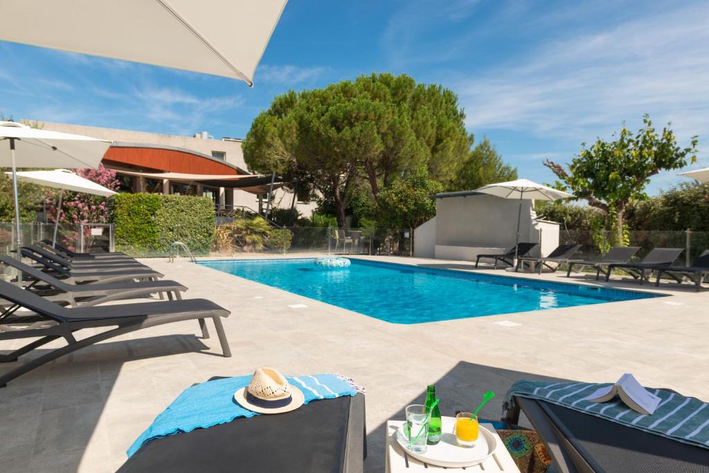 a swimming pool with chaise lounges and umbrellas at Kyriad Montpellier Est - Lunel in Lunel