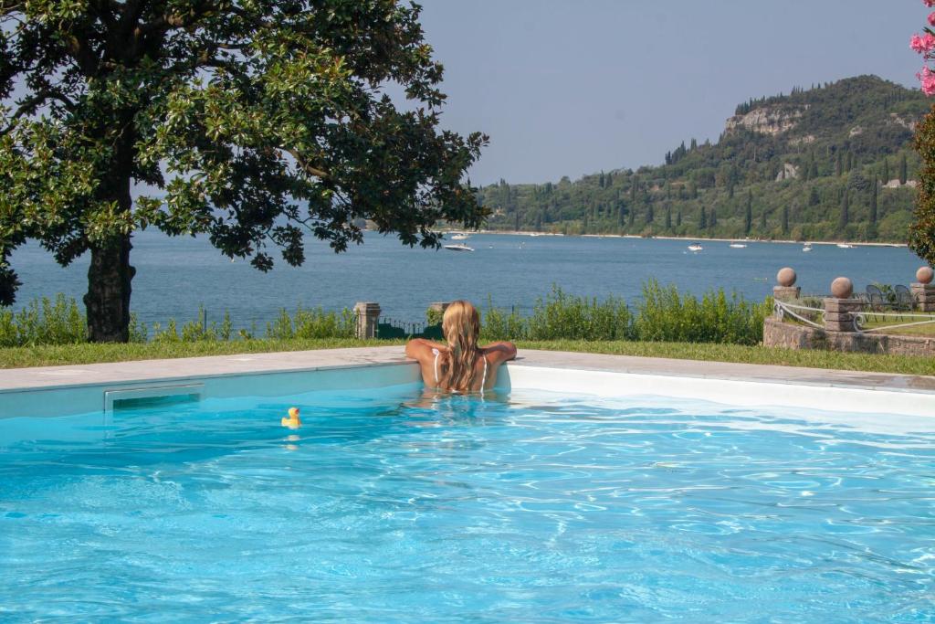 a woman in a swimming pool with a view of the water at Appartamenti Villa Andrea in Garda