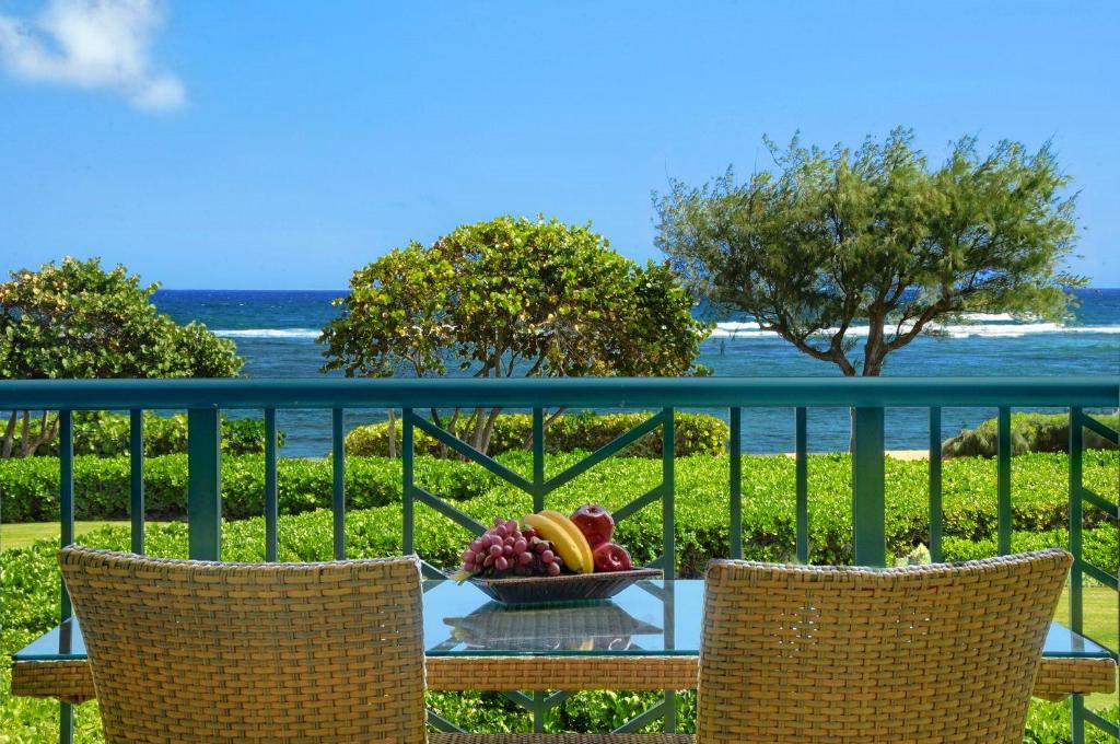 a table with a bowl of fruit on a balcony at Waipouli Beach Resort Spectacular Luxury Oceanfront Condo Sleeps 8 AC Pool in Kapaa