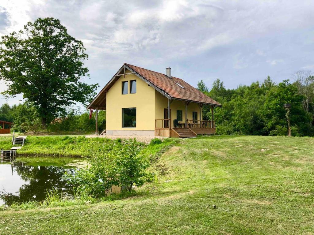 uma pequena casa amarela numa colina com um lago em Guesthouse Sidrabozoli em Līči