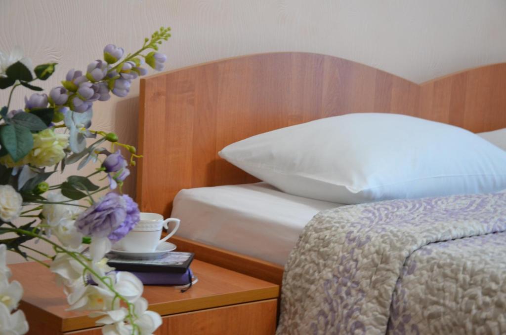 - une chambre avec un lit et un vase de fleurs sur une table dans l'établissement Отель "Евразийский", à Rostov-sur-le-Don