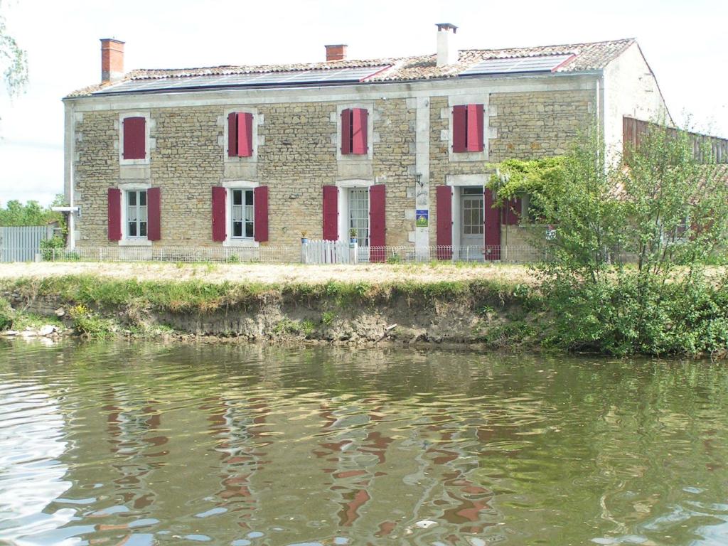 una vieja casa de ladrillo con persianas rojas y un cuerpo de agua en Au Bord de Sèvre, en Coulon