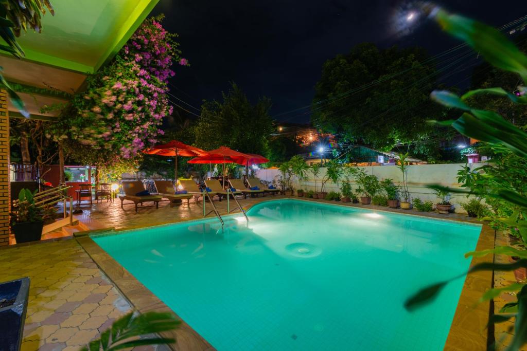 a swimming pool at night with chairs and umbrellas at Five Rose Siem Reap Hostel in Siem Reap