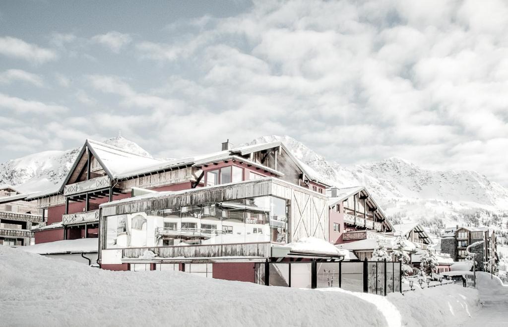 a building in the snow with mountains in the background at Hotel Rigele Royal Superior in Obertauern