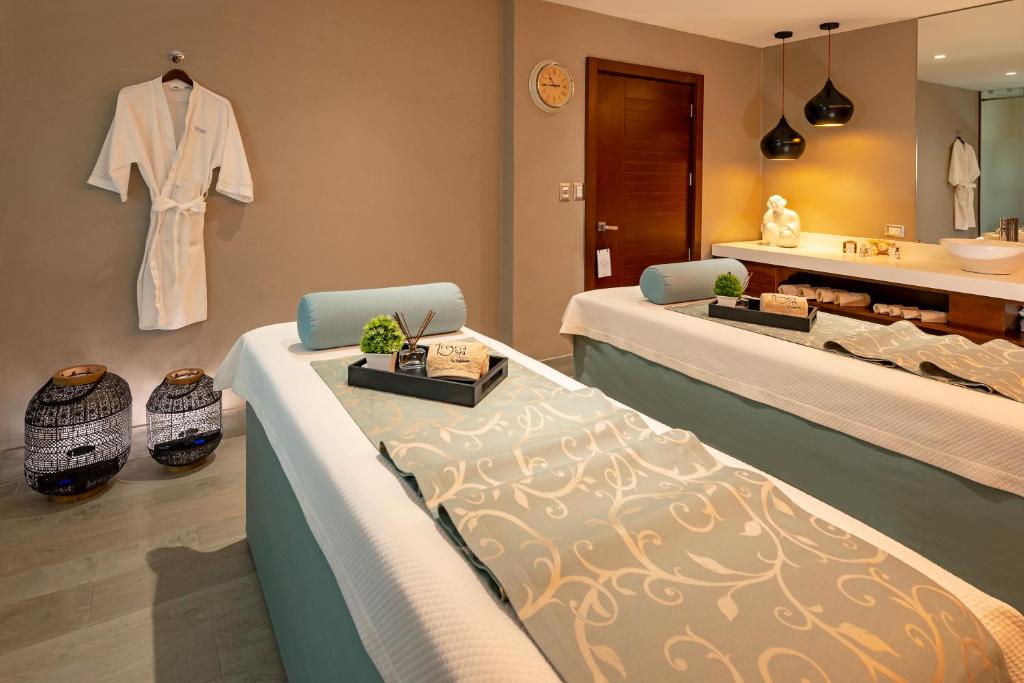 two beds in a bathroom with a sink and a robe at Catalonia Santo Domingo in Santo Domingo