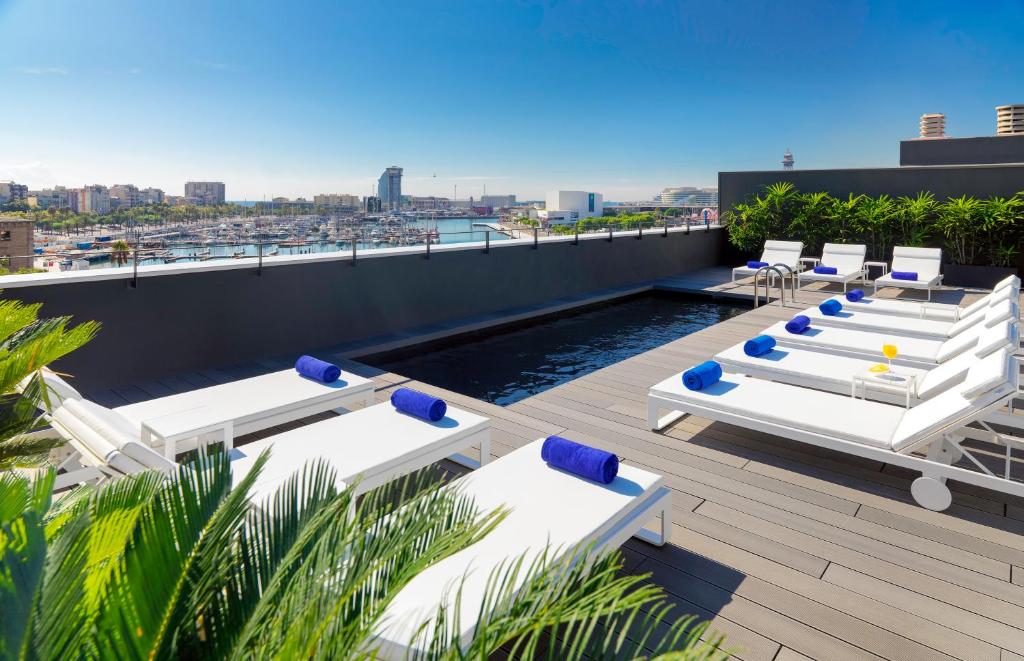 una terrazza panoramica con sedie a sdraio bianche e una piscina di H10 Port Vell 4* Sup a Barcellona
