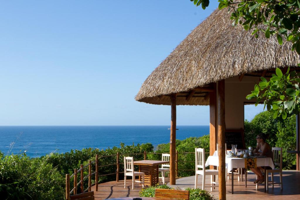 een restaurant met een tafel en stoelen en de oceaan bij Dunes de Dovela eco-lodge in Chefe Chume