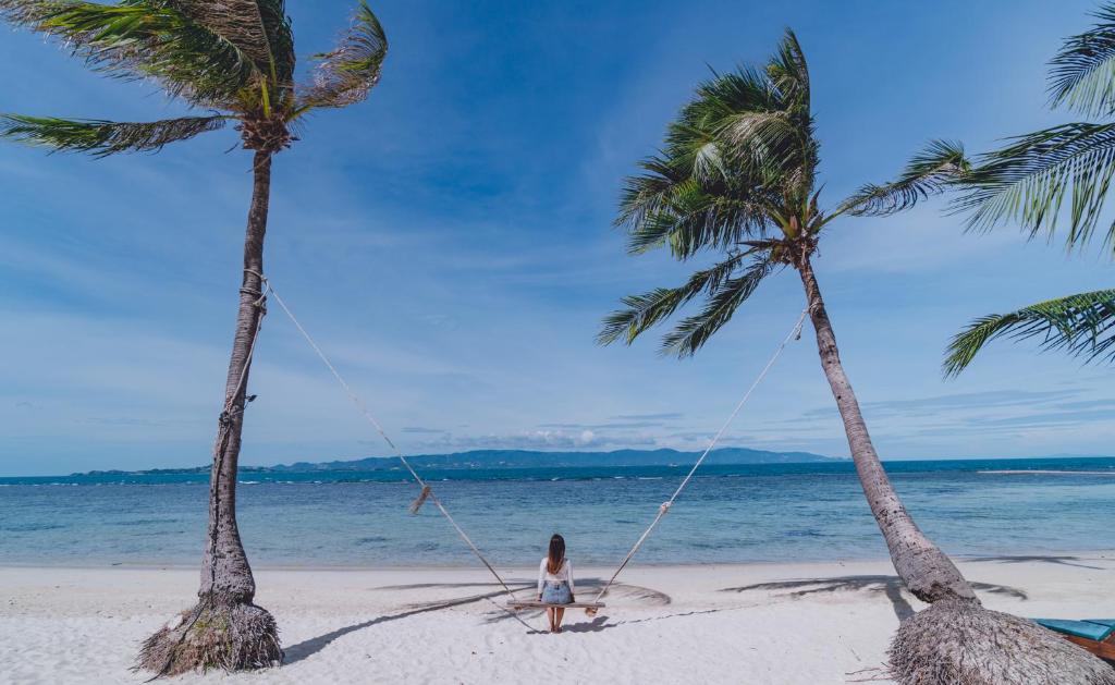 a girl on a swing between two palm trees on a beach at Cocohut Beach Resort Koh Phangan in Haad Rin