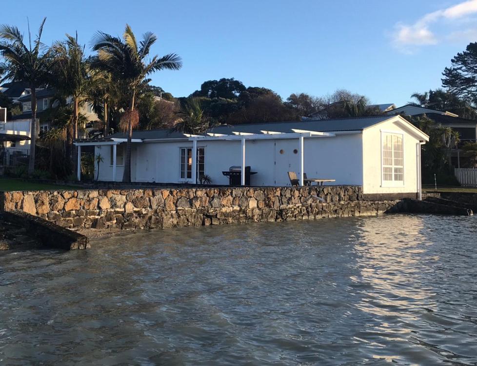 una casa sull'acqua vicino a un muro di pietra di The Boat House ad Auckland