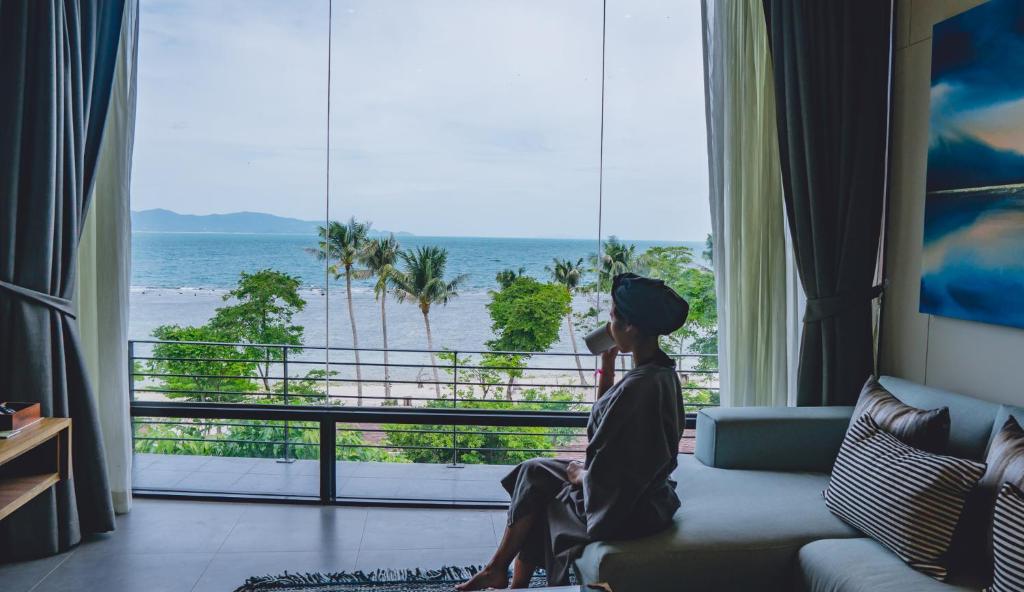 a woman sitting on a couch looking out a window at the ocean at The Cabin Beach Resort in Haad Rin