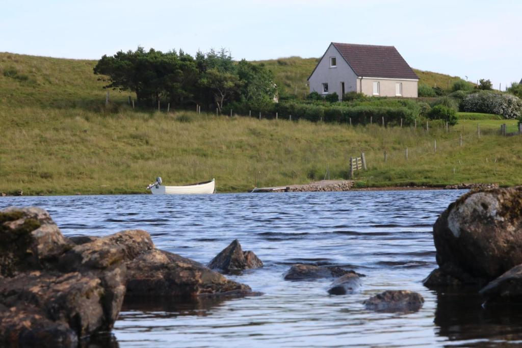 a boat in the water with a house in the background at Grey Goose Cottage in Lochs