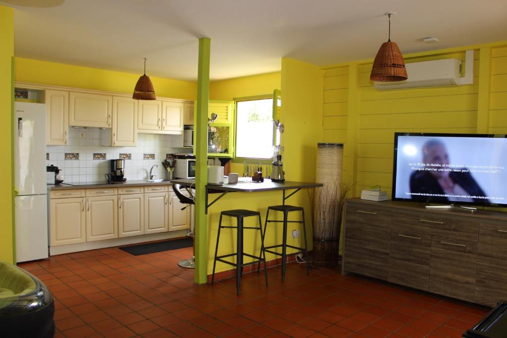 une cuisine aux murs jaunes, une table et une télévision dans l'établissement VILLA SOKA, à Les Anses-d'Arlet