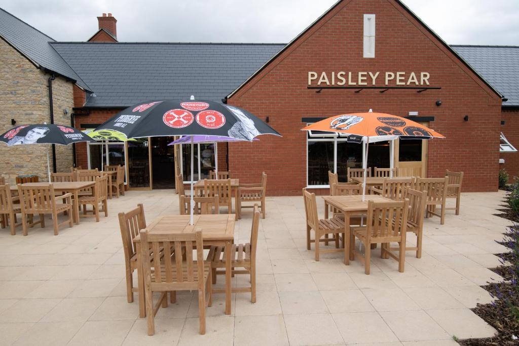 eine Terrasse mit Tischen und Sonnenschirmen vor einem Restaurant in der Unterkunft Paisley Pear, Brackley by Marston's Inns in Brackley