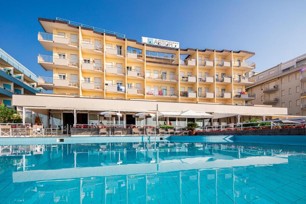 un hôtel avec une piscine en face d'un bâtiment dans l'établissement Hotel Astor, à Lido di Jesolo