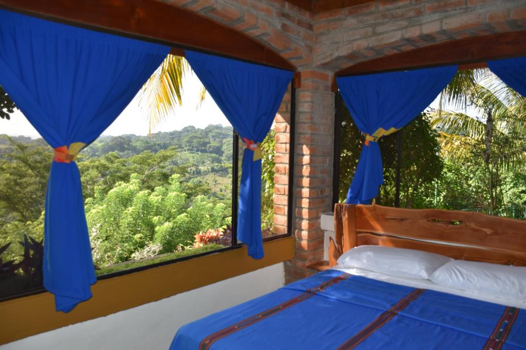 1 dormitorio con 1 cama y una ventana con cortinas azules en The Mayan Grouper, en Suchitoto