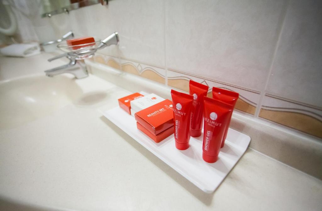 a white bathroom sink with red toothbrushes and toothpaste at AZIMUT Hotel Siberia in Novosibirsk