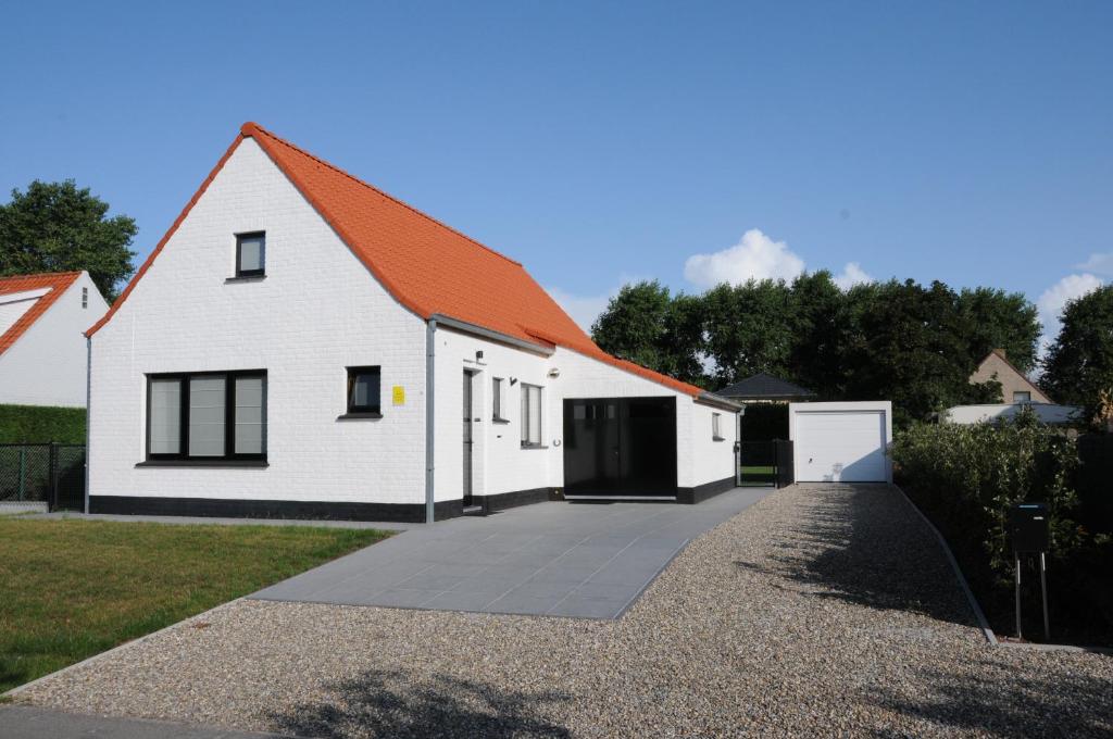 une maison blanche avec un toit orange et une allée. dans l'établissement Villa KARIN, à Oostduinkerke