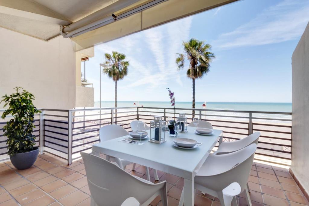 een witte eettafel en stoelen op een balkon met uitzicht op het strand bij Apartamento La Terraza del Mar in Cádiz