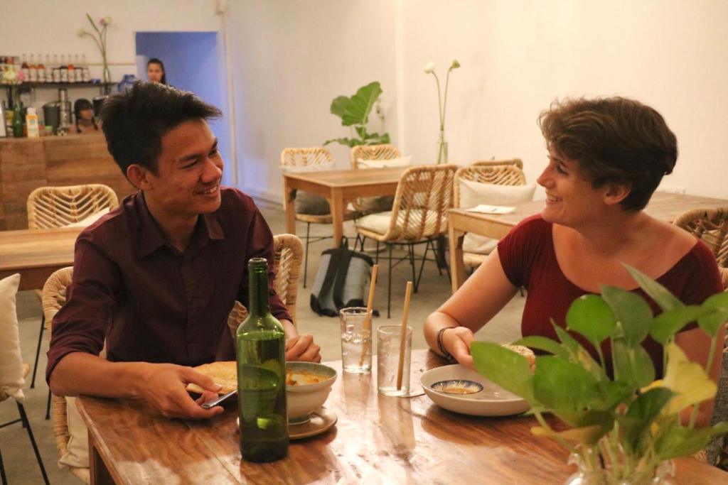 Sacred Lotus - Vegan Café X Hostel في بنوم بنه: يجلس شخصان على طاولة مع زجاجة من النبيذ