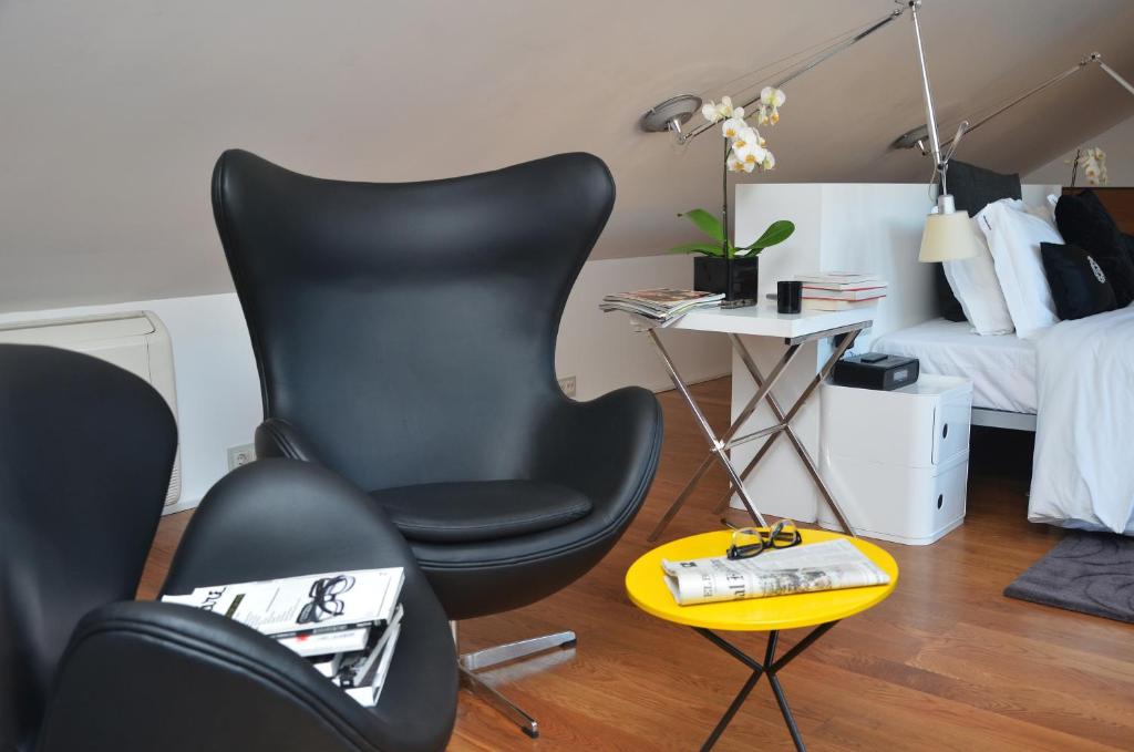 A bedroom corner with a black lounge chair, compact desk, magazines and a yellow side table.